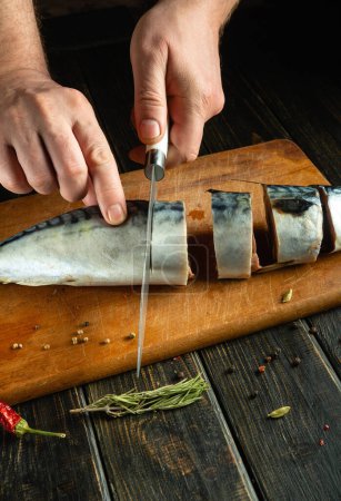Las manos del hombre cortan la caballa en la tabla de la cocina antes de freír. El concepto de preparar un plato de pescado para la cena.