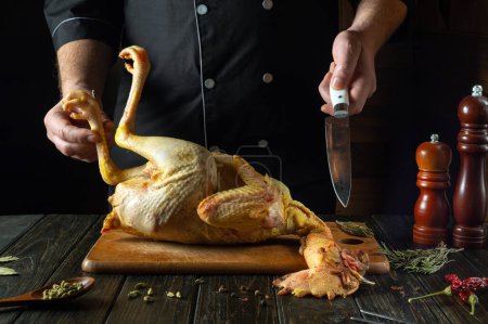 Foto de Un plato de pollo crudo a manos de un chef en la cocina de una casa pública. Concepto de cocinar gallo crudo en una tabla de cortar. Cuchillo en la mano de un cocinero. - Imagen libre de derechos