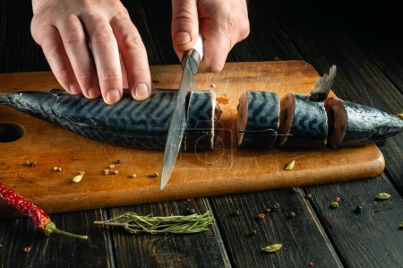 Cortar pescado antes de cocinar con un cuchillo en las manos de un chef. El cocinero corta la caballa en una tabla de cortar antes de freírla para la cena..