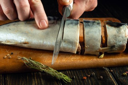 Cooking salted mackerel on a kitchen board. A knife for slicing fish in the hands of a cook.