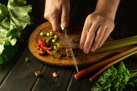 The cook hands using a knife to cut rheum plant on a kitchen board before preparing vitamin salad for lunch. Vegetarian dish cooking concept.