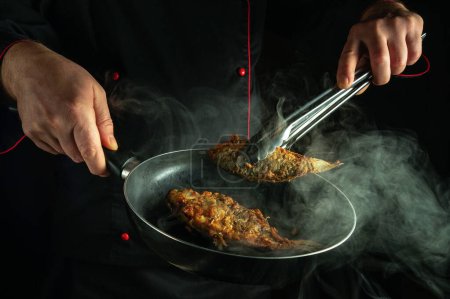 Ein professioneller Koch frittiert in der Küche Fisch. Das Konzept, ein Fischgericht zum Abendessen zuzubereiten. Die Hand des Kochs entfernt mit einer Zange scharf gebratene Kakerlaken aus der Pfanne.