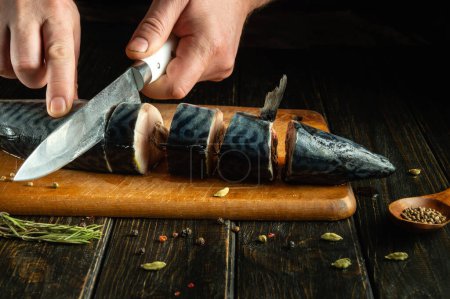 Cortar el pescado de caballa en una tabla de cocina con un cuchillo en la mano del chef antes de freírlo. Lugar para la publicidad en un fondo negro.