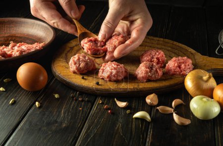 Male hands make meatballs on the kitchen table with minced meat and a spoon. Concept of cooking for dinner at home.
