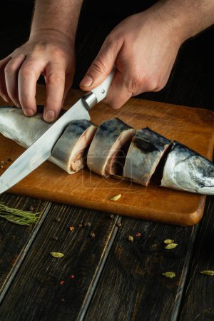 Fischscheiben mit einem Messer in der Hand eines Kochs für die Zubereitung des Abendessens auf dem Küchentisch.