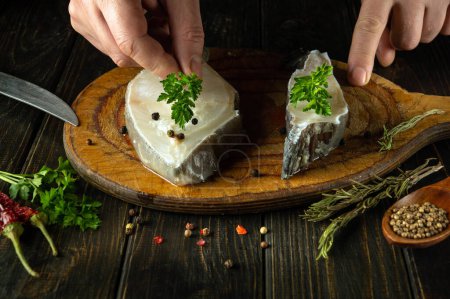 Primer plano de las manos de un chef añadiendo perejil aromático al pescado Anarhichas antes de freír. El concepto de una deliciosa dieta de pescado en un restaurante.