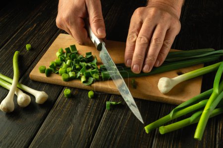 Frischen Knoblauch mit einem Messer in den Händen eines Küchenchefs auf einem Schneidebrett schneiden. Low-Key-Konzept der Zubereitung von Gemüsesalat. Werbefläche.