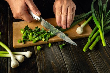 A man hands cut young garlic with a knife on a cutting board. Making vegetable salad at home. Advertising space.