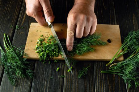 Dill oder Fenchel mit einem Messer in der Hand auf dem Küchentisch pflücken, um ein schmackhaftes Abendessen zuzubereiten. Kopierraum.