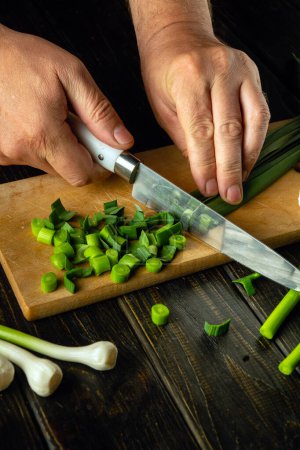 The cook hands using a knife to cut green garlic on a cutting board for preparing a vegetarian dish or salad. Place for advertising.