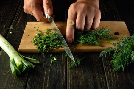 Close-up of a chef hands using a knife to chop fresh dill before adding it to food for aroma and taste. Space for advertising.