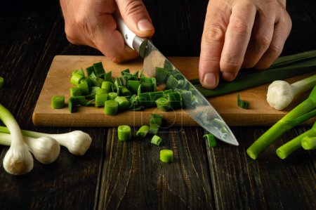 Chef hands chop green garlic with a knife on a cutting board for vitamin salad. Diet menu for breakfast or dinner. Advertising space.