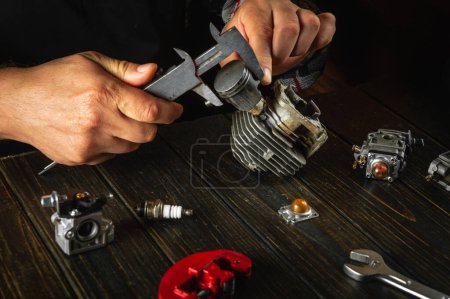 Ein Reparaturmeister an seinem Schreibtisch in der Werkstatt repariert nach einer Panne den Motor eines Rasenmähers. Messung des Kolbendurchmessers in einem Motorzylinder mit Bremssattel.