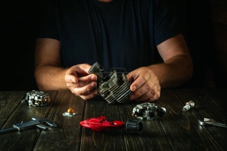 Ein Mechaniker in einer Werkstatt repariert den Motor eines Rasenmähers oder Trimmers. Das Konzept der Reparatur und Restaurierung von Motoren nach einer Panne.