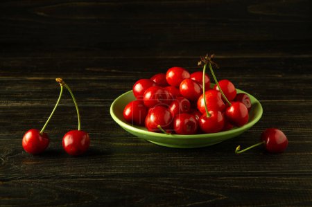 Green plate full of fresh ripe sweet cherries on dark antique table. Prunus avium rich harvest concept.