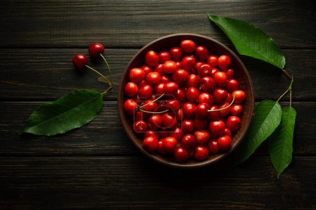 Fresh ripe sweet cherries in a bowl and leaves on a black table. The concept of healthy eating and a rich cherry harvest.