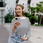 Pretty good-looking girl with smartphone in hands and wearing headphones is enjoying music and looking aside with happy smile 