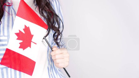 Téléchargez les photos : Étudiante non reconnue en chemise bleue blanche tenant un petit drapeau canadien sur fond gris, fête du Canada, jour férié, vote, immigration, taxe, espace de copie. - en image libre de droit