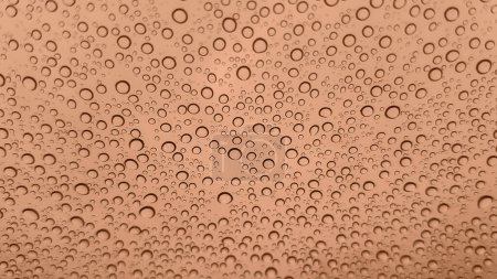 Abstract image of rain drops on glass. Image toned in Peach Fuzz color of the year 2024. New Fashion color. Top view. Abstract drops view
