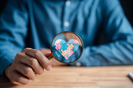Photo for Man hold magnifier focus Awareness heart jigsaw puzzle, Color puzzle symbol of awareness for autism spectrum disorder family support. Autism World Awareness Day. - Royalty Free Image
