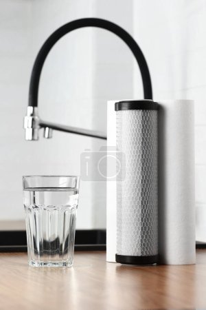 Photo for A glass of clean fresh water and set of filter cartridges on wooden table in a kitchen interior. Installation of reverse osmosis water purification system. Concept Household filtration system - Royalty Free Image