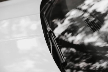 Téléchargez les photos : Gros plan de la vue de face du pare-brise de voiture blanc moderne propre avec réflexion de la nature, essuie-glaces, gros plan sur un thème de voiture. Nouveau luxe extérieur. - en image libre de droit