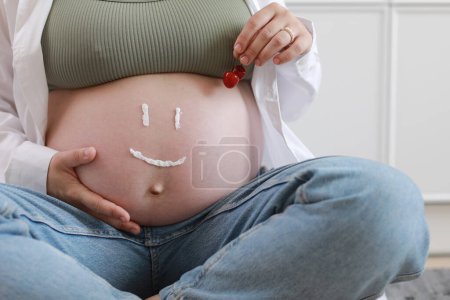 Photo for Close-up of torso of young pregnant model applying moisturizer on her belly to avoid stretch marks. Future mom with funny smile from moisturizing cream on her tummy. Pregnancy skincare concept. - Royalty Free Image