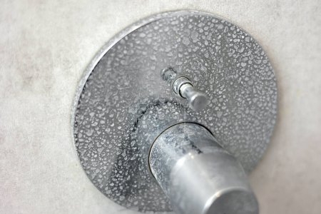 Dirty calcified shower mixer tap, faucet with limescale on it, plaque from hard water, Chrome plated shower, close up photo. Bathroom with grey tiles interior