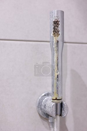 Dirty calcified shower chrome mixer tap, faucet with limescale on it, plaque from hard water. Steel plumbing with fungus, mildew, close up. Bathroom with grey tiles interior. Domestic life concept.
