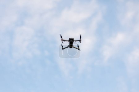 Téléchargez les photos : Drone volant sur ciel bleu avec fond de nuages blancs. Vue du bas Quadcopter avec appareil photo numérique. Télécommande volante Quadrocopter, UAV - en image libre de droit
