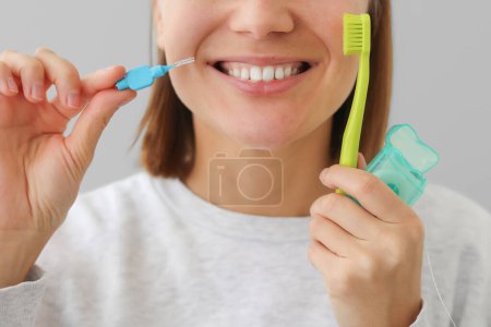 Téléchargez les photos : Femme méconnaissable avec des dents blanches tient fil dentaire, brosse à dents et brosse interdentaire pour prévenir la maladie buccodentaire. Dentisterie de soins de santé et concept d'hygiène buccodentaire.. - en image libre de droit