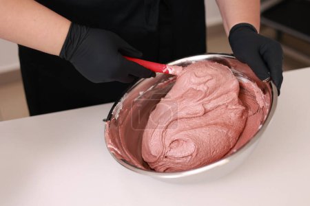 The pastry chef mixes silicone spatula the brown dough for the French desert macaron or macaroon in a stainless steel bowl, the process of preparing the cakes. Concept of confectionery or pastry shop.