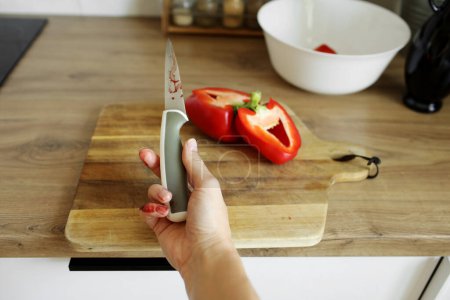 Foto de La mujer se cortó el dedo meñique con un cuchillo mientras cocinaba ensalada de verduras en la cocina. La mano femenina con un cuchillo de retención de sangre con una cuchilla afilada resultó en un accidente de cocción de dedos cortado y herido - Imagen libre de derechos