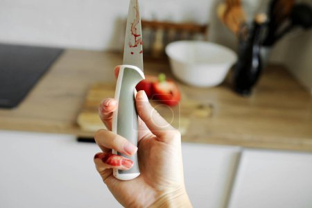 Foto de La mujer se cortó el dedo meñique con un cuchillo mientras cocinaba ensalada de verduras en la cocina. La mano femenina con un cuchillo de retención de sangre con una cuchilla afilada resultó en un accidente de cocción de dedos cortado y herido - Imagen libre de derechos