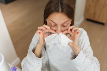 Allergie, Grippe, Erkältung, Schnupfen. Lustiges Gesicht einer kranken Frau mit Papiertaschentüchern in der Nase vor laufender Nase und Niesen zu Hause. Heuschnupfen, Sinusitis und Virusinfektion im Taschentuch.