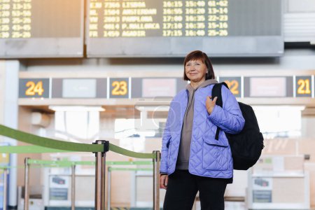 Photo for Middle aged woman traveler with backpack at public airport terminal after check in at airline services desks. Active retirees. Travelling, vacation, tourism concept - Royalty Free Image