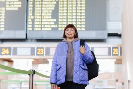 Photo for Middle aged woman traveler with backpack at public airport terminal after check in at airline services desks. Active retirees. Travelling, vacation, tourism concept - Royalty Free Image