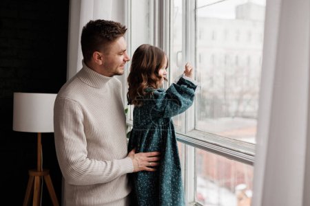 Fathers day. Happy loving young dad embracing adorable little daughter by the window at home. Happy family of two enjoy spend time together. Childcare, custody, reunion after long separation concept.