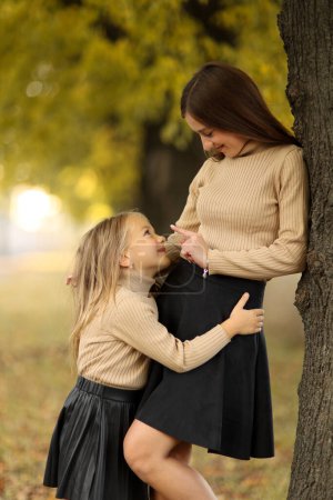 Familientag. Junge Mutter und kleine Tochter haben Spaß und erholen sich im herbstlichen Park. Entzückendes Kindermädchen umarmt und küsst ihre Mutter. Mütterliche Fürsorge und Liebe zum Kind. Muttertag.