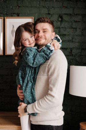Happy Father's Day. Smiling young dad embraces with big hug his adorable little child daughter at home. Single daddy and small kid hug cuddle enjoy sweet moments together. Fatherhood. Children's day.