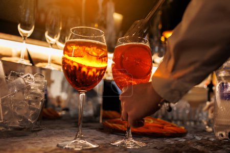 Bartender makes two glasses of cocktail Aperol spritz on bar counter, adds fresh orange slices. Typical alcoholic Italian beverage, aperitif made with Prosecco sparkling white wine and ice cubes