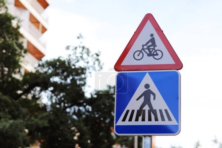 Warning red triangular bicycle sign above square pedestrian crossing sign outdoors on city street. Traffic safety regulations. Cyclists may appear, intersection with cycle path outside intersection.