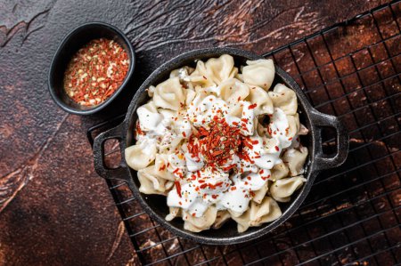 Foto de Cooking Manti Dumpling with yoghurt and tomato sauce in a skillet. Dark background. Top view. - Imagen libre de derechos