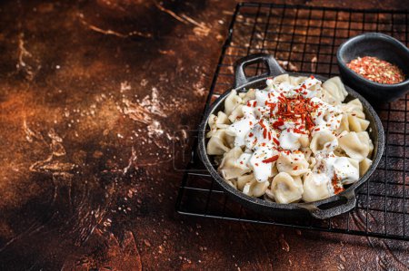 Foto de Cooking Manti Dumpling with yoghurt and tomato sauce in a skillet. Dark background. Top view. Copy space. - Imagen libre de derechos