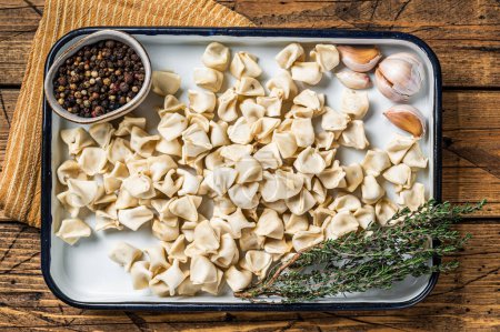 Foto de Raw Manti Dumpling with meat in tray with herbs and spices. Wooden background. Top view. - Imagen libre de derechos