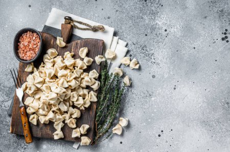 Foto de Uncooked Manti Dumpling on wooden board with herbs, raw food. Gray background. Top view. Copy space. - Imagen libre de derechos