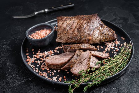 Téléchargez les photos : Barbecue wagyu vieilli sec Tri Tip steak de boeuf sur une assiette avec du sel rose. Fond noir. Vue du dessus. - en image libre de droit