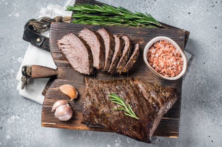Téléchargez les photos : Rôti et tranché steak de bœuf tri pointe sur une planche en bois avec des herbes. Fond gris. Vue du dessus. - en image libre de droit