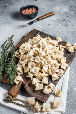 Foto de Uncooked Manti Dumpling on wooden board with herbs, raw food. Gray background. Top view. - Imagen libre de derechos