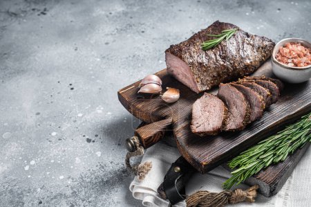 Téléchargez les photos : Roast and sliced tri tip beef steak on a wooden board with herbs. Gray background. Top view. Copy space. - en image libre de droit